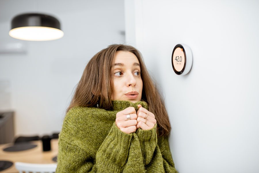 Premier AC & Heating LLC | Rock Hill, SC | young woman cold in her home, staring at thermostat